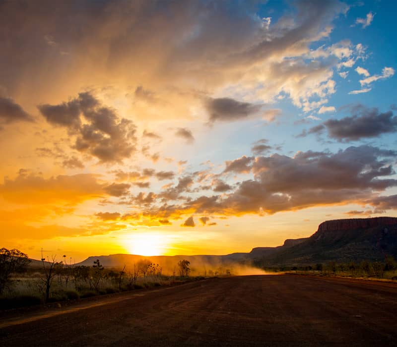 An unpaved road through the Kimberley outback at sunset with mountains in the background, Western Australia.