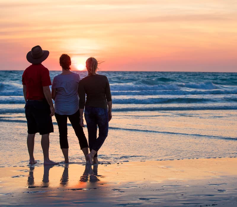 Three people silhouetted against a golden sunset on Cable Beach in Broome, Western Australia.