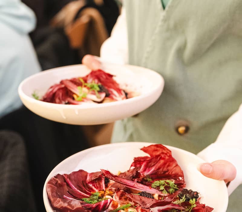 A server carrying two gourmet plates of fresh salad with dark berries and radicchio in a Hunter Valley restaurant.