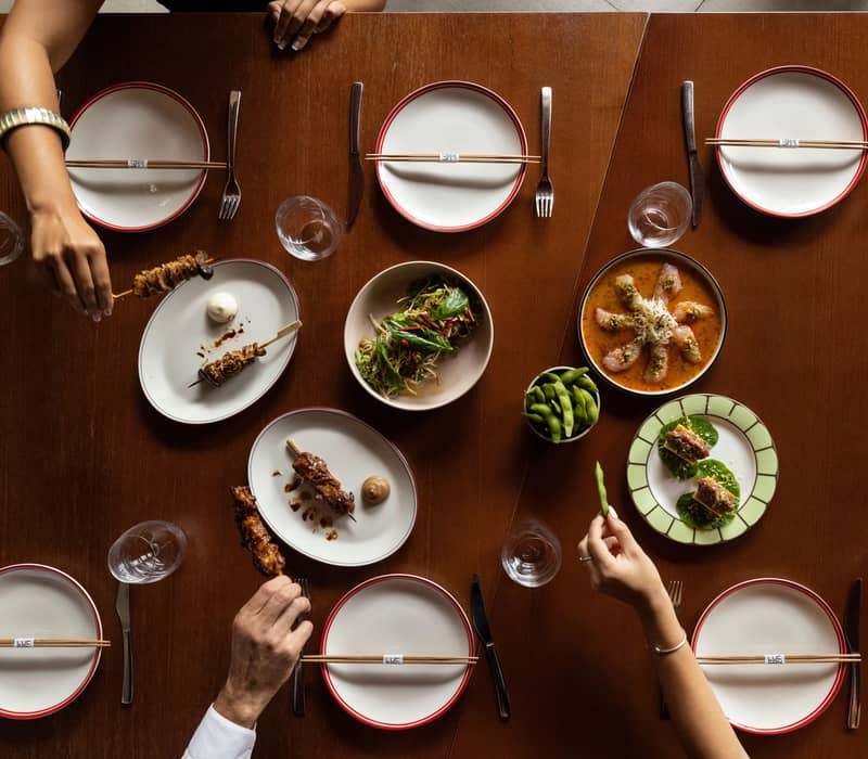 Top-down view of a wooden table set with various small plates of Asian food and chopsticks.
