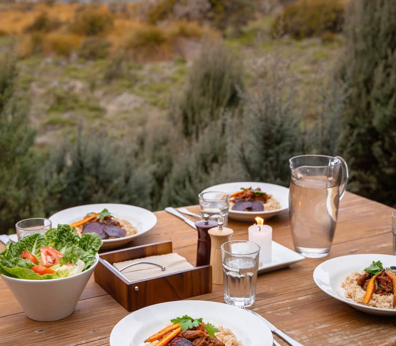 Gourmet dinner served on a wooden table outdoors with a view of Tasmanian mountains and scrub.