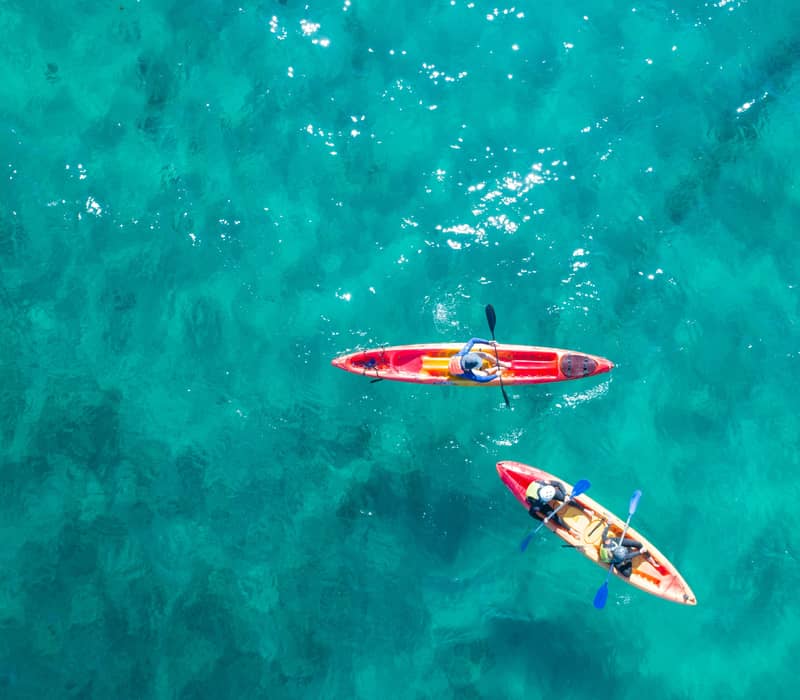 Overhead view of two red kayaks paddling through crystal clear tropical water.