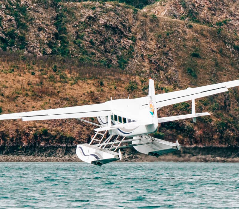 White seaplane in mid-takeoff from the ocean against a backdrop of rugged Kimberley mountains.