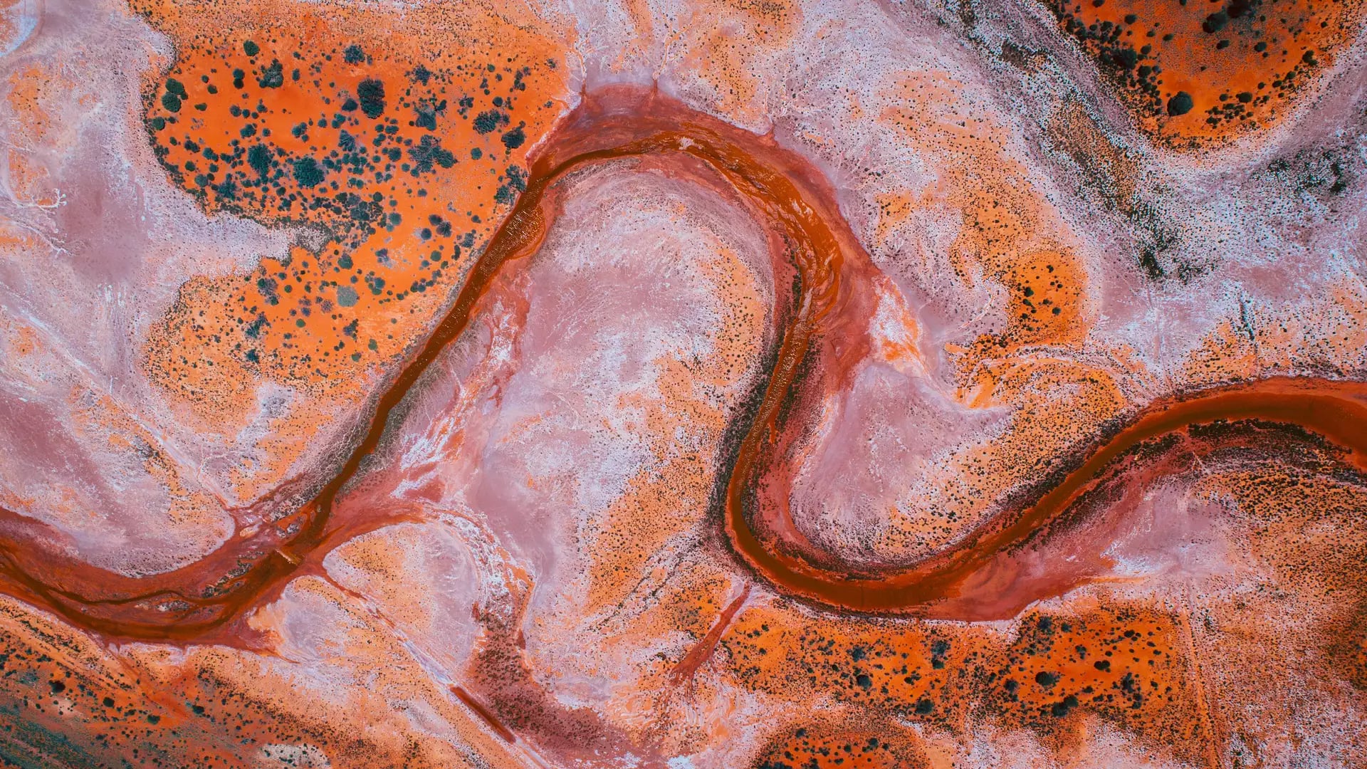 Abstract swirls of deep orange, pink, and white create a natural pattern on the floor of a salt lake in the Kalgoorlie and Goldfields region of Western Australia.