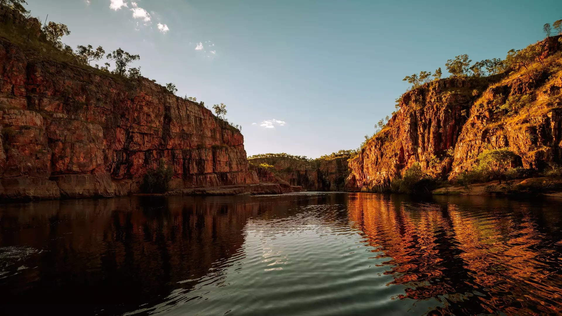 A low-angle water perspective of the first gorge at Nitmiluk National Park, captured as the rising sun casts a golden glow on the vertical sandstone faces.
