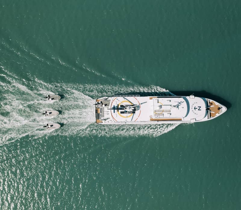 An aerial top-down view of the flagship expedition vessel True North cruising through the deep green waters.