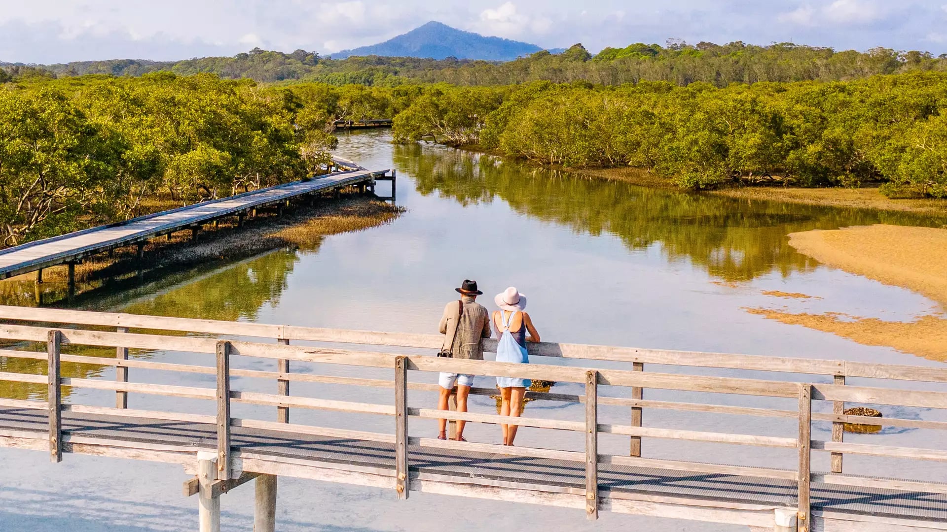Travelers standing on a wooden boardwalk over shallow turquoise water in Urunga, NSW.