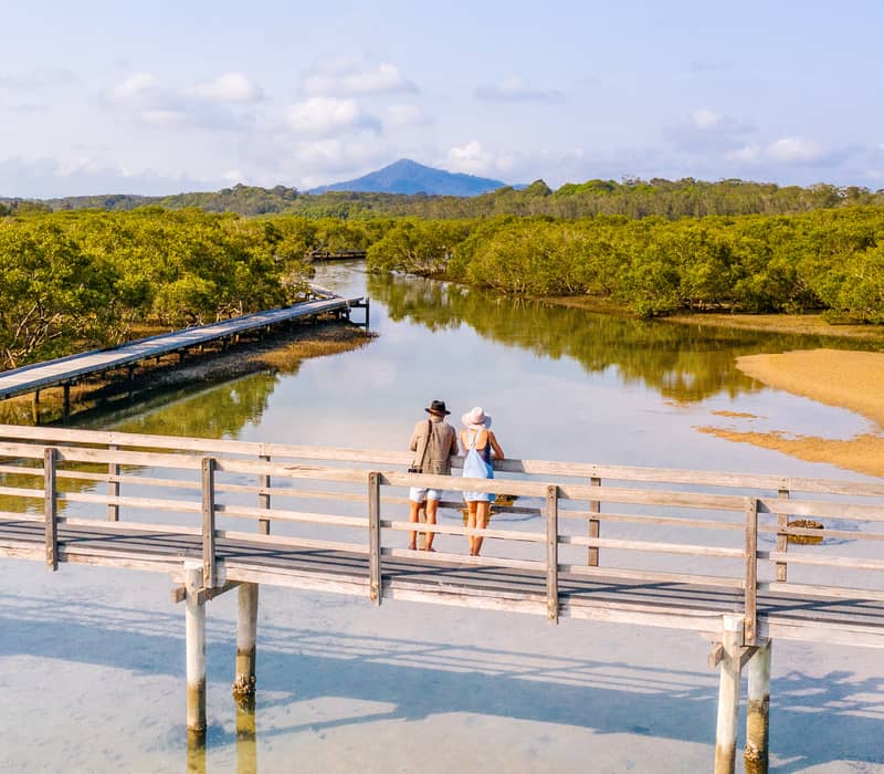 Travelers standing on a wooden boardwalk over shallow turquoise water in Urunga, NSW.