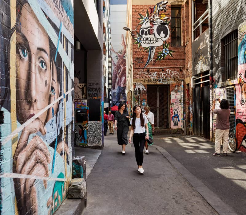 Tourists walking through a narrow Melbourne laneway covered in colorful street art and murals.