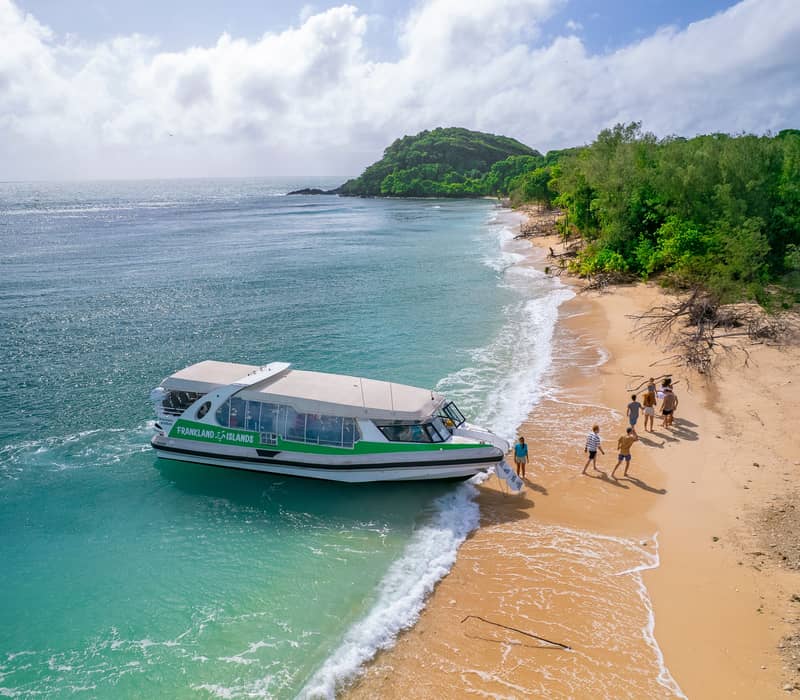 Aerial view of a tour boat on the shore of Frankland Islands with tourists on the beach.