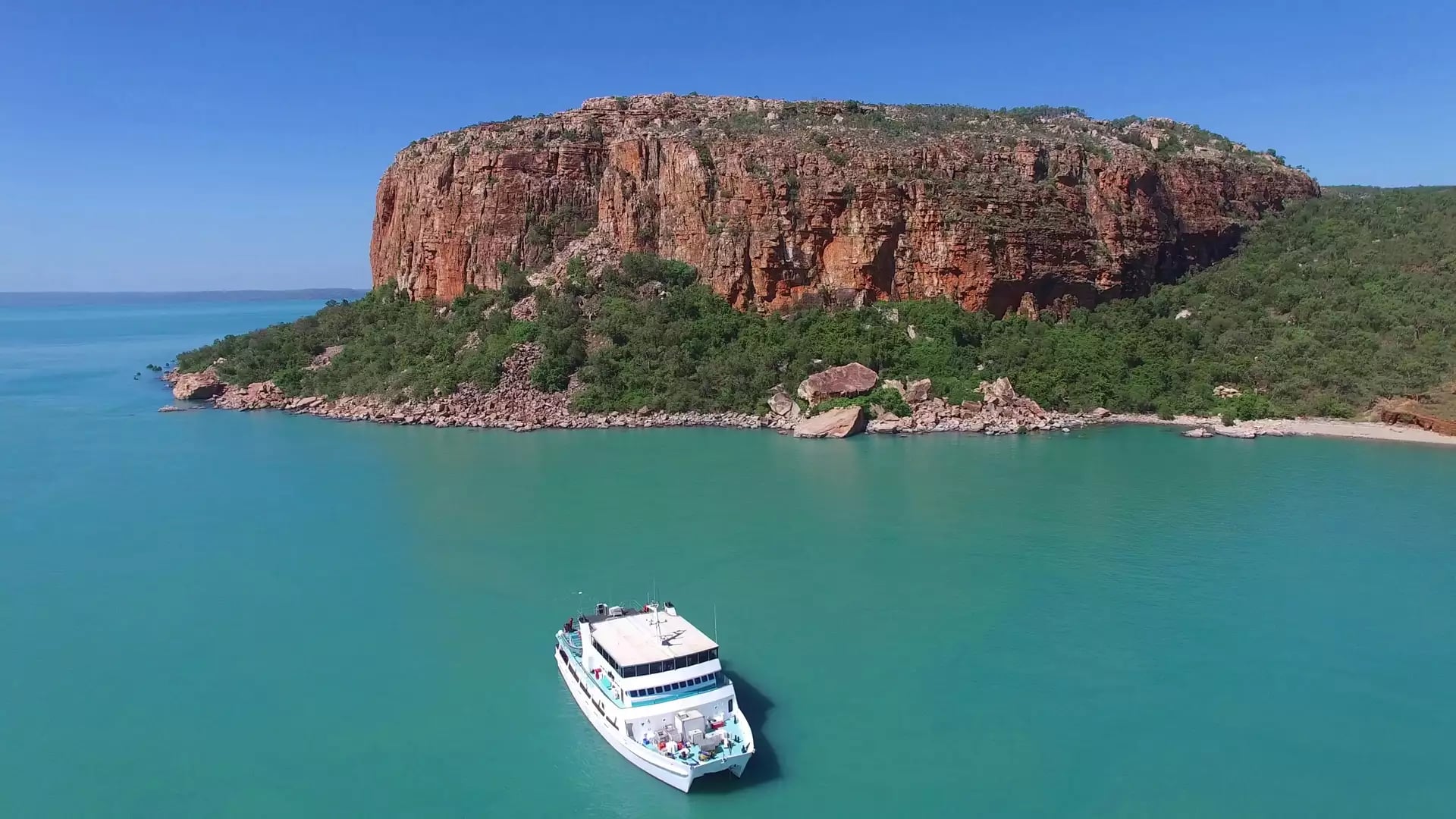 An Eco Abrolhos Cruise vessel sits in the turquoise waters beside a dramatic flat-topped island in Western Australia.