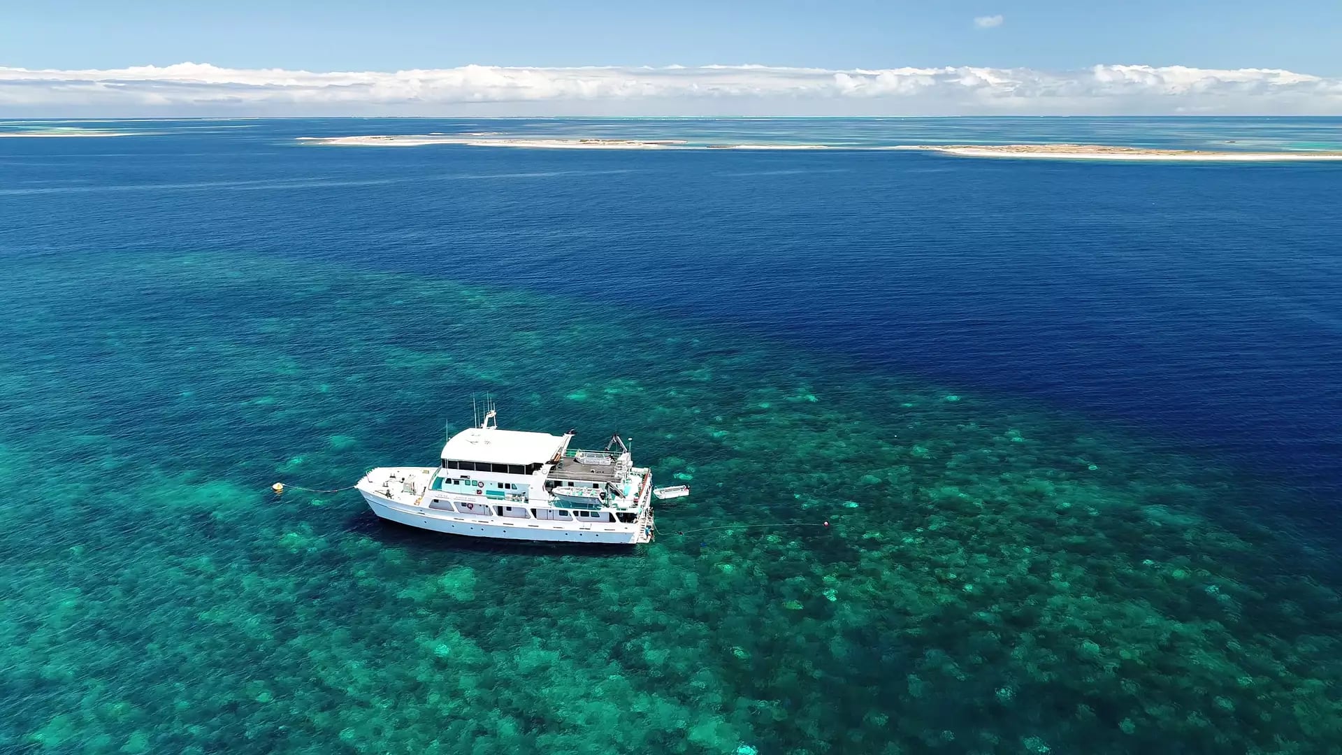 An aerial view of an Eco Abrolhos Cruise vessel anchored in the vibrant, turquoise coral reefs of Western Australia.