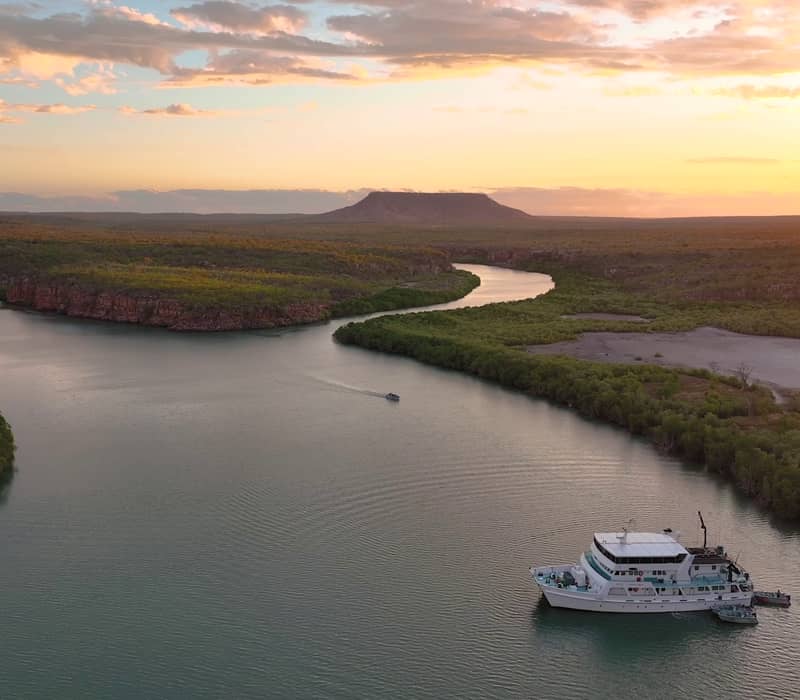 A golden sunset glows over an Eco Abrolhos Cruise ship anchored at the Three Ways river junction in Western Australia.