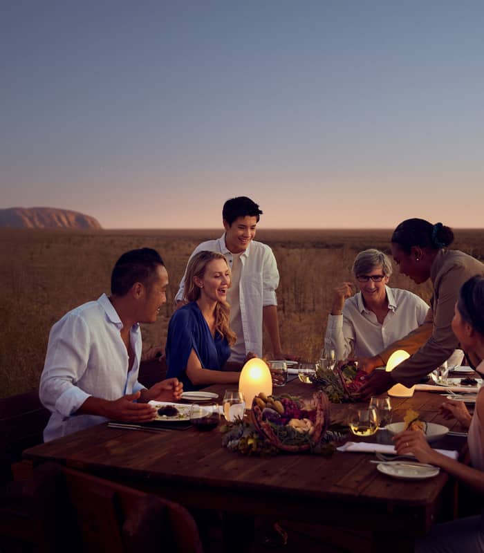 A group of friends laughing at a luxury outdoor dinner table in the Australian outback.