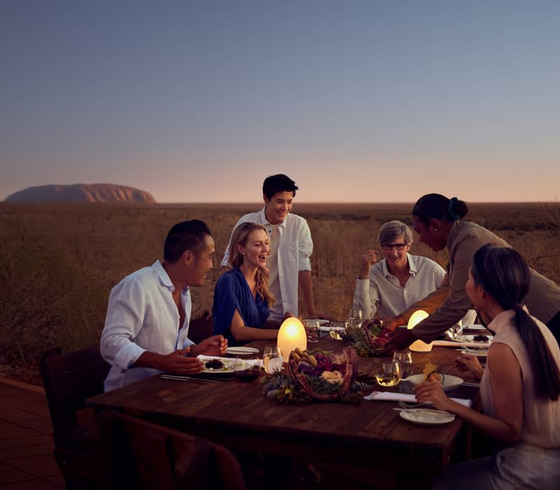 A group of friends laughing at a luxury outdoor dinner table in the Australian outback.