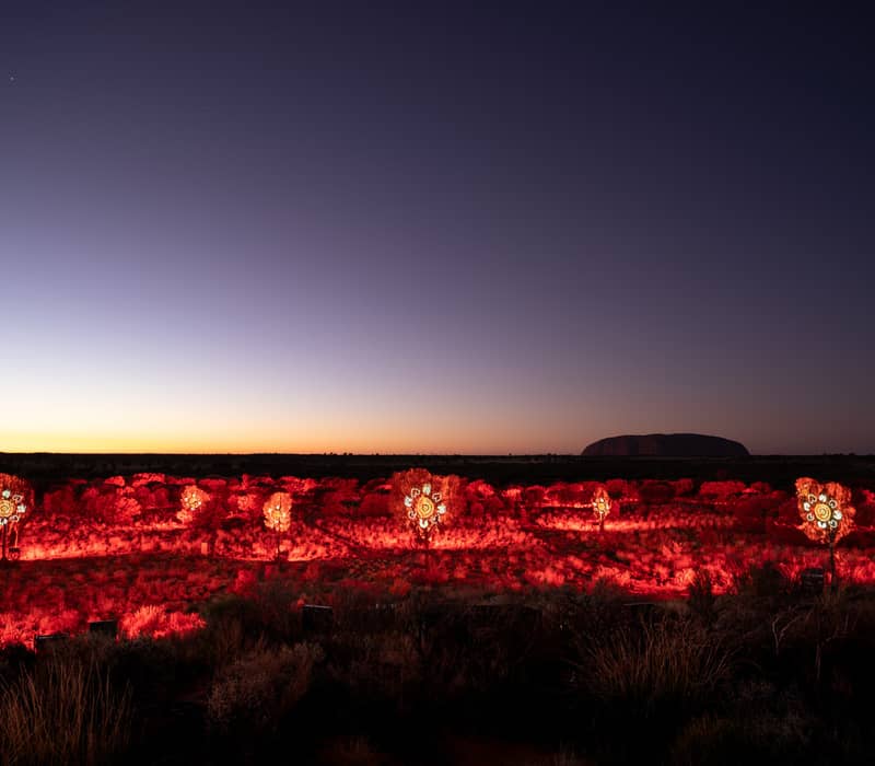 Red glowing Indigenous light art installations in the desert at dawn near Uluru.