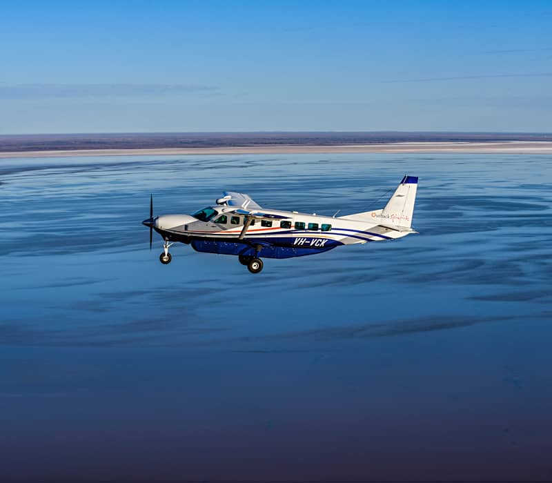 An Outback Spirit private charter aircraft soaring over the vast, shimmering expanse of Kati Thanda–Lake Eyre during the historic 2025–2026 flood event.