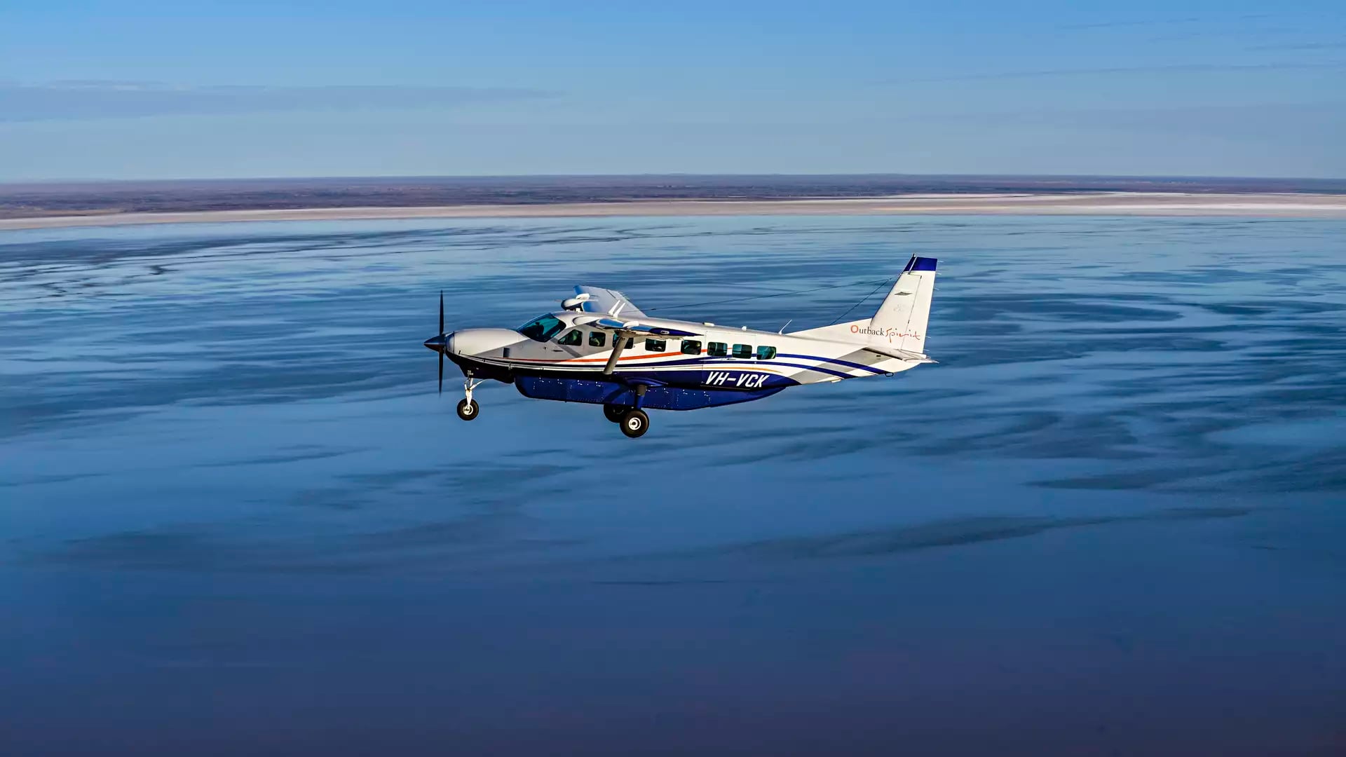 An Outback Spirit private charter aircraft soaring over the vast, shimmering expanse of Kati Thanda–Lake Eyre during the historic 2025–2026 flood event.