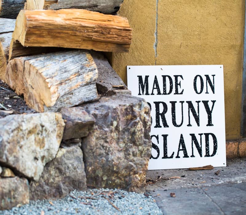 Bruny Island Cheese Co sign propped up against a Yellow wall and an array of chopped fire logs.