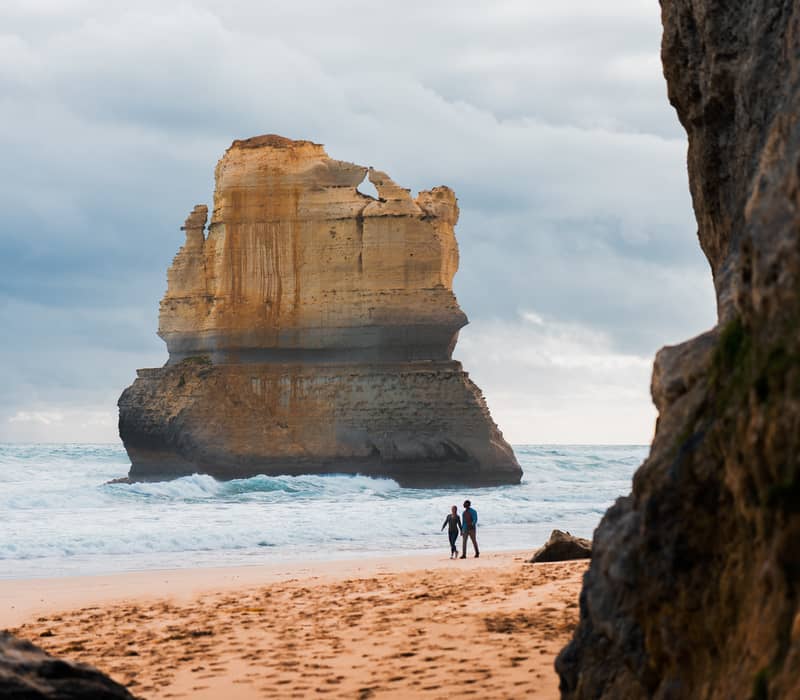 Two people walking on the beach next to a massive limestone sea stack at the Twelve Apostles, Victoria.