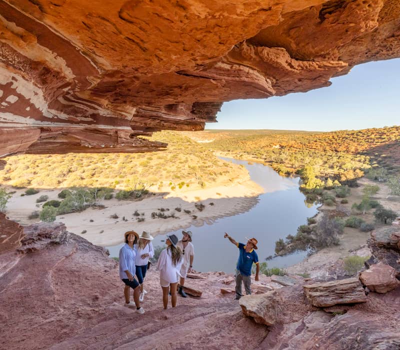 A tour guide pointing out landscape features to a small group inside a red sandstone rock overhang.