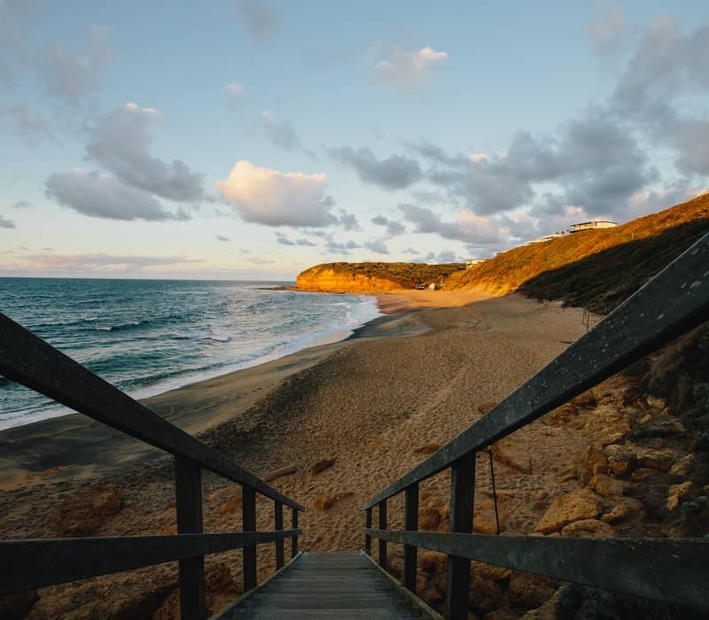 A wooden staircase leading down to a sandy beach at sunset on the Victorian coastline.