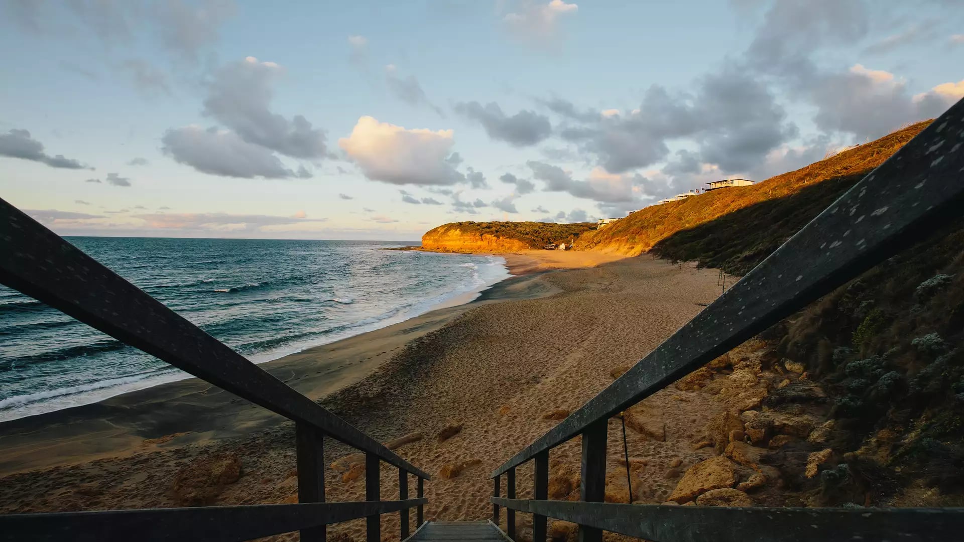 A wooden staircase leading down to a sandy beach at sunset on the Victorian coastline.