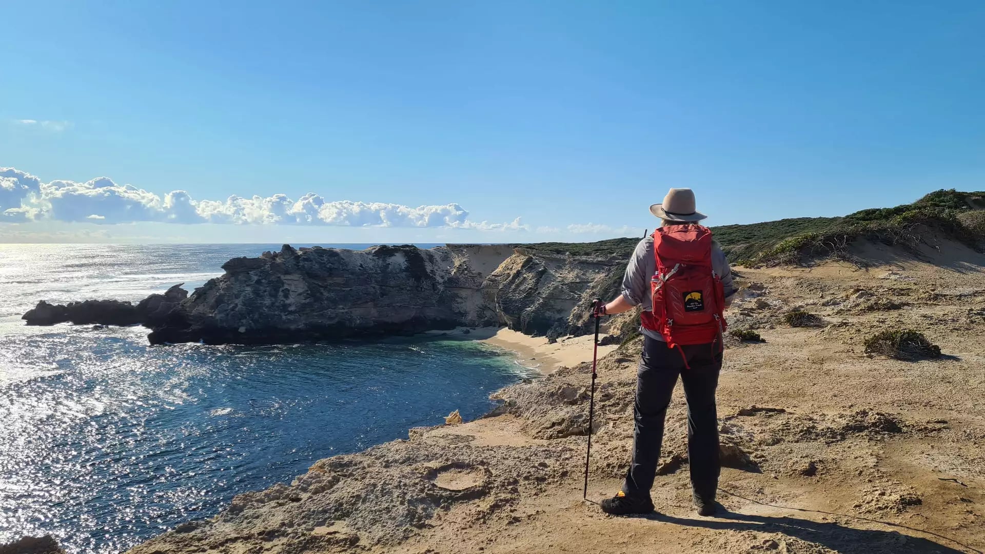 Hiker with a red pack looking down at the pristine white sands and blue water of Horseshoe Bay.