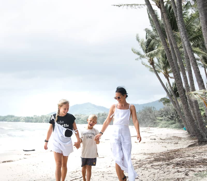 A happy family walking along the beach in Palm Cove under tropical palm trees in North Queensland.