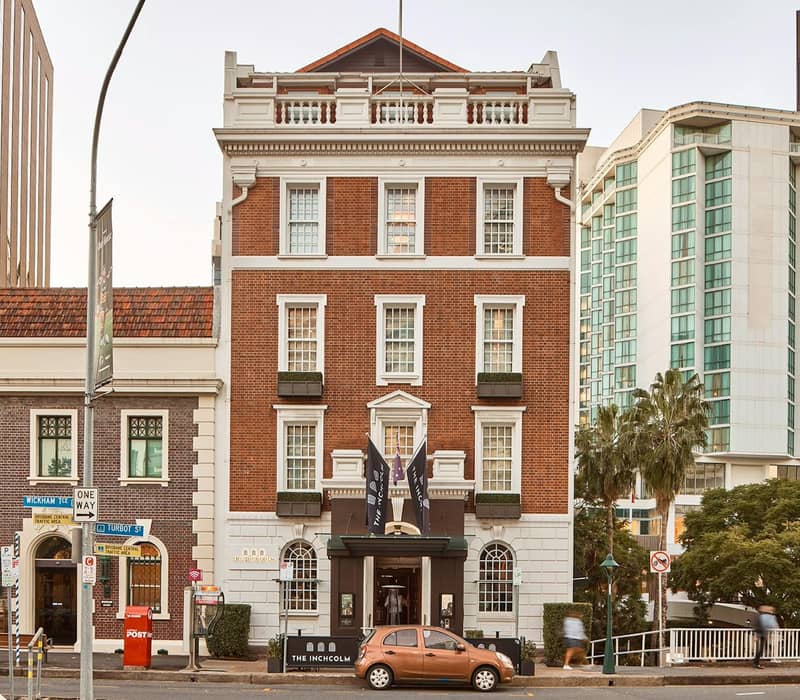 Historic brick hotel building with flags outside, parked car and nearby modern buildings in the city.