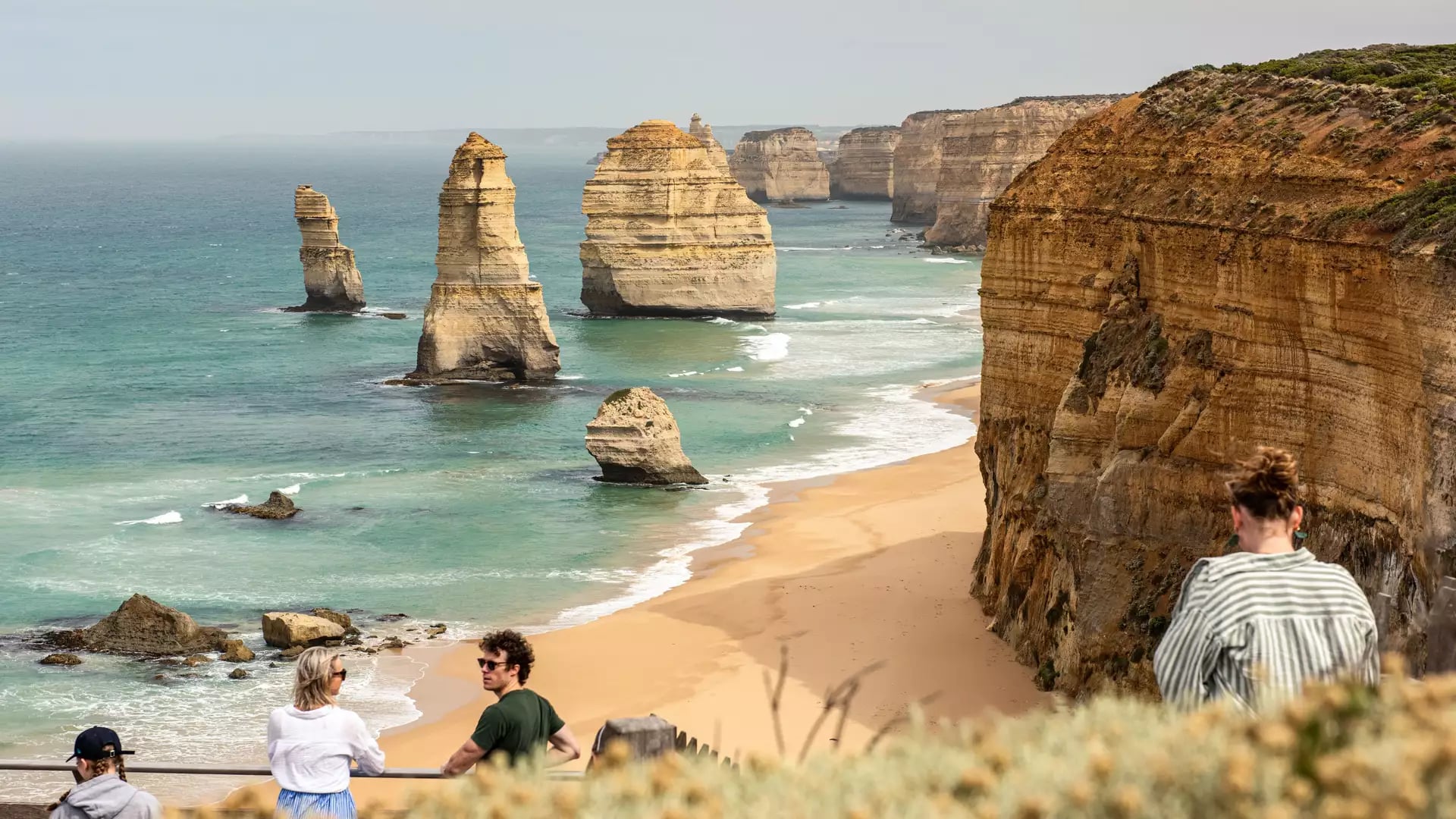 Tourists looking out over the Twelve Apostles limestone stacks and turquoise ocean on the Great Ocean Road, Victoria.