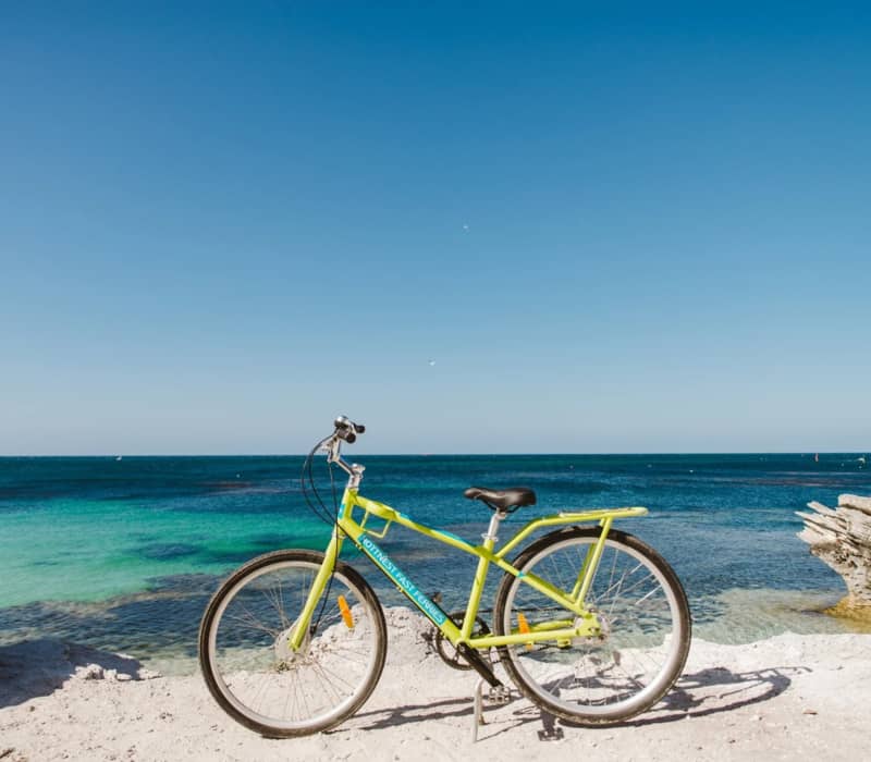 A lime green bicycle parked on a sandy limestone cliff overlooking the turquoise ocean at Rottnest Island.