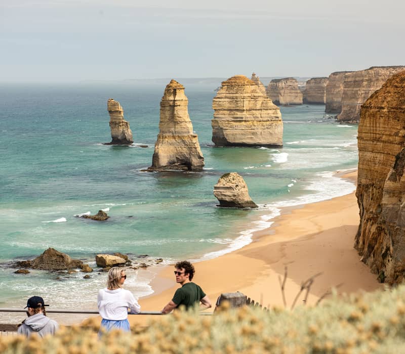 Tourists looking out over the Twelve Apostles limestone stacks and turquoise ocean on the Great Ocean Road, Victoria.