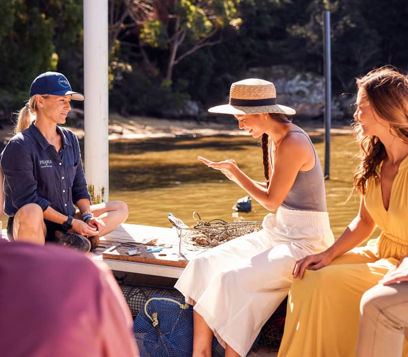 A travel group examines a freshly harvested pearl on a wooden dock at Broken Bay Pearl Farm, NSW.