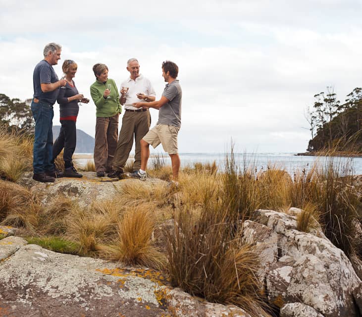 Group of travelers enjoying fresh oysters and wine on the coast of Bruny Island, Tasmania.