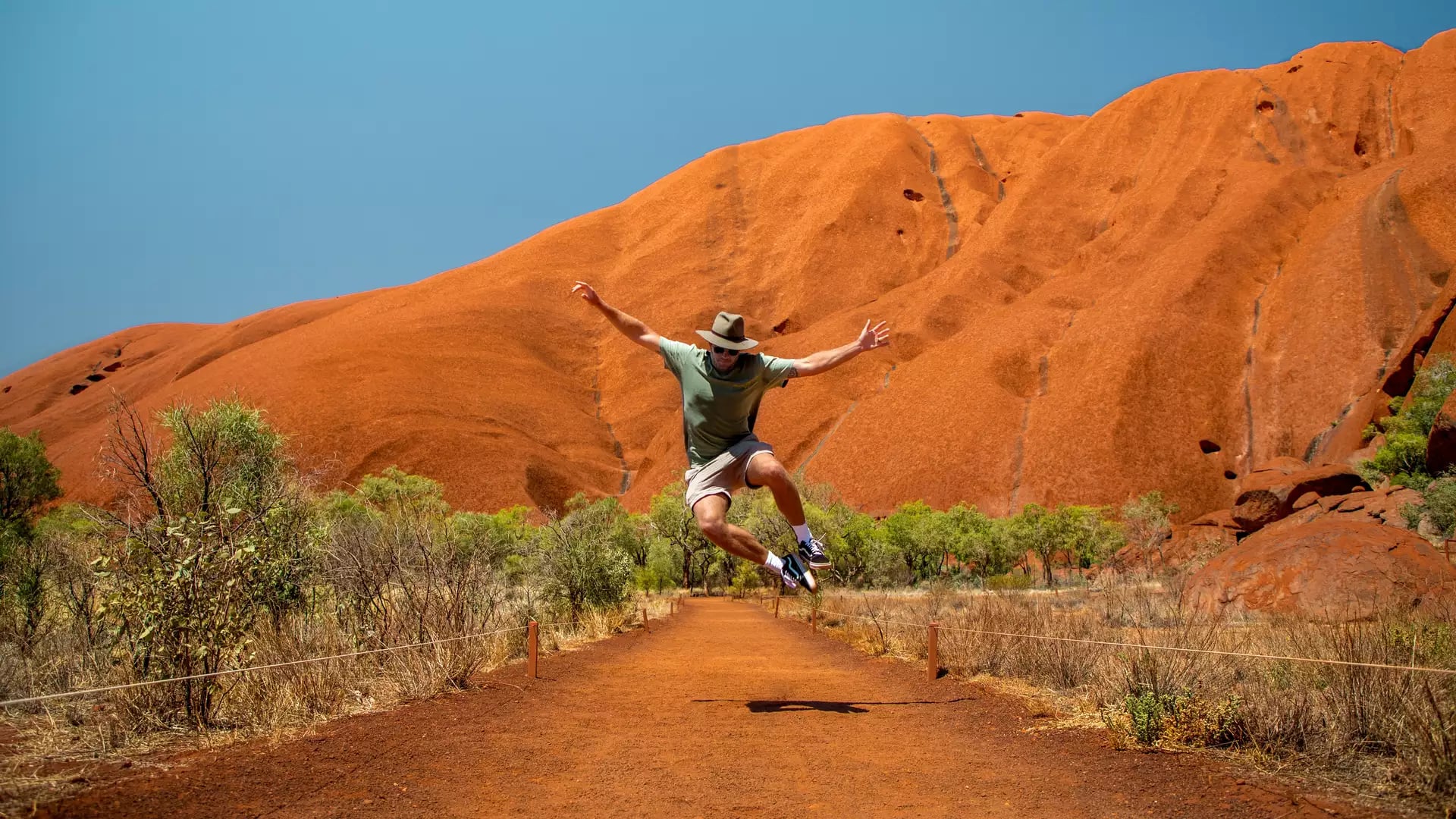 A man jumping for joy on a hiking path at the base of Uluru, Northern Territory, Australia.