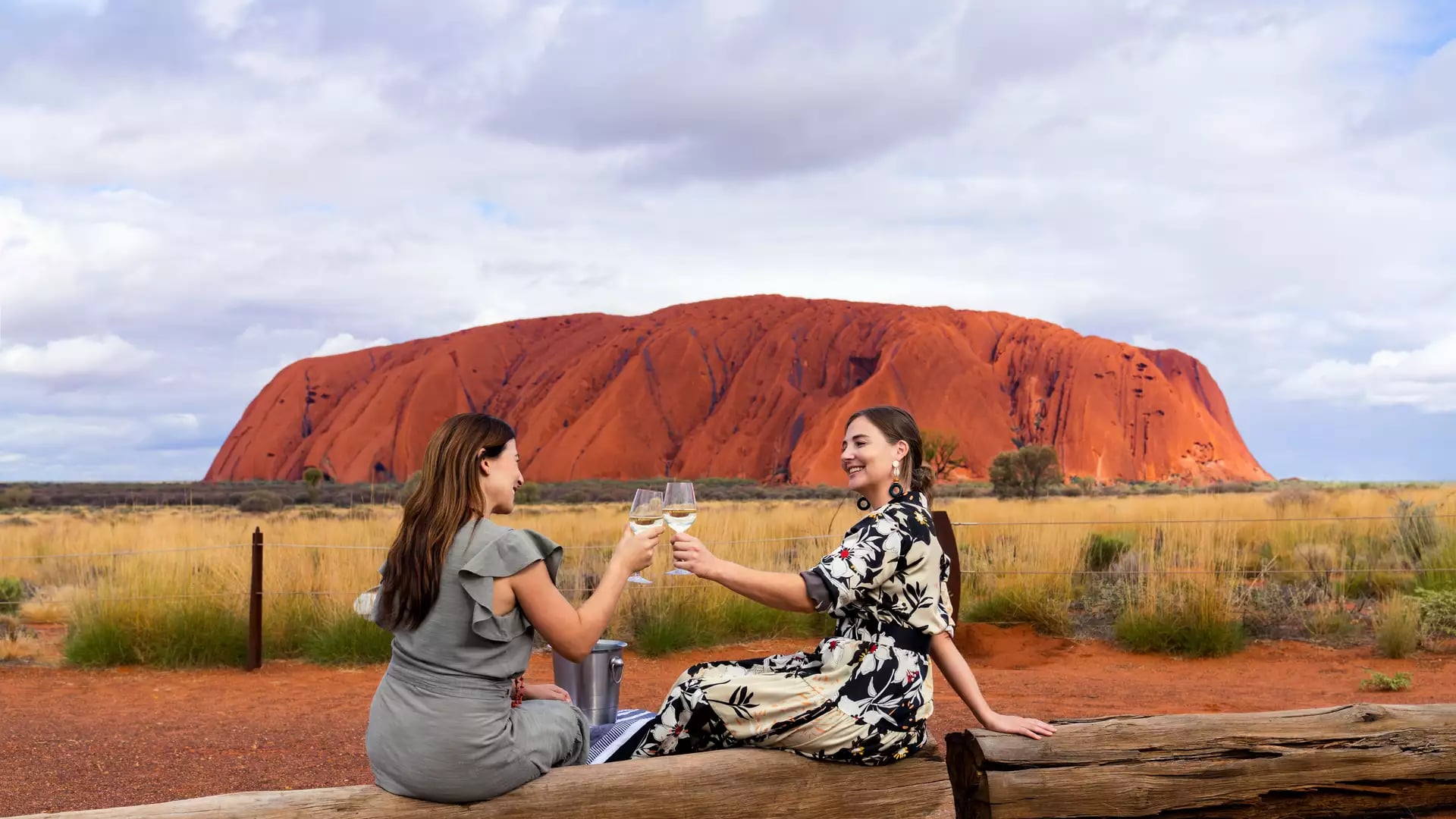 Two women toasting with wine glasses at sunset in front of Uluru, Northern Territory, Australia.