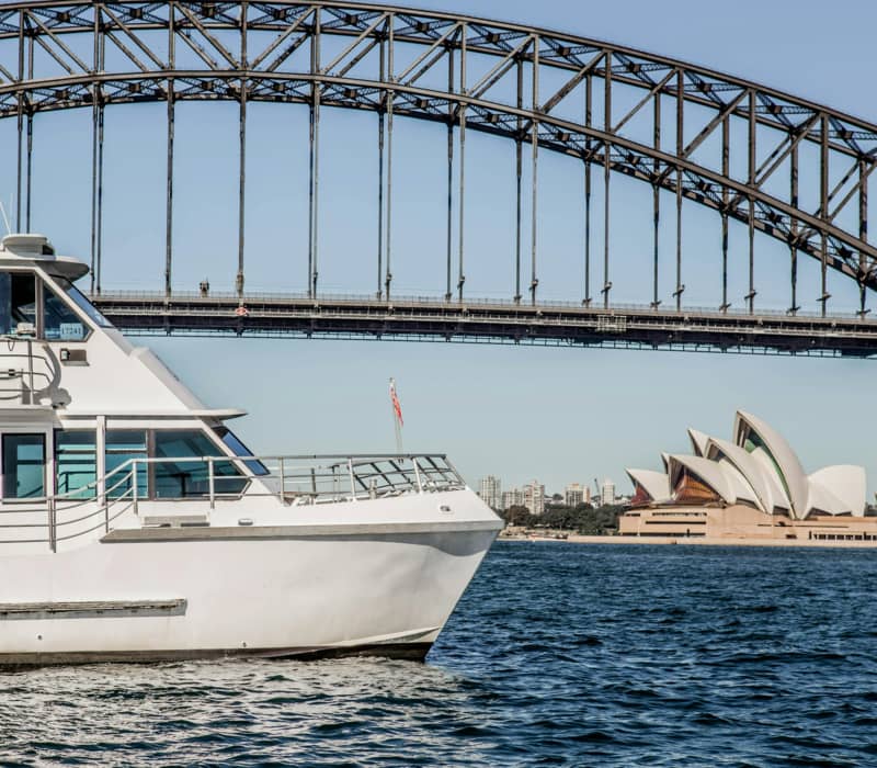 A white cruise boat on Sydney Harbour with the Sydney Harbour Bridge and Opera House in the background.