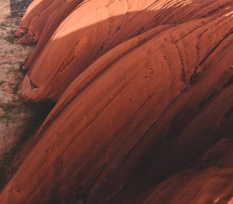 Looking down on the steep, grooved red slopes of Uluru showing the intricate patterns of erosion and shadow.