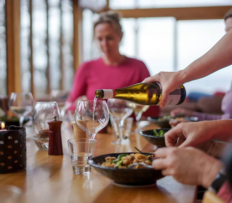 Close-up of white wine being poured into a glass during a communal dinner at a luxury lodge.