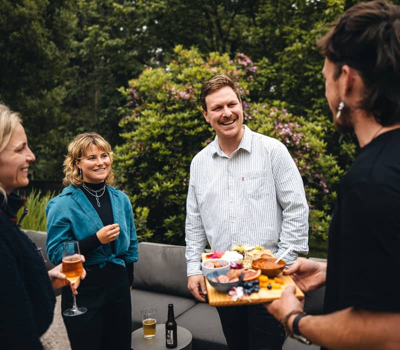 Four people laughing and sharing a cheese platter and wine outdoors at a luxury lodge.