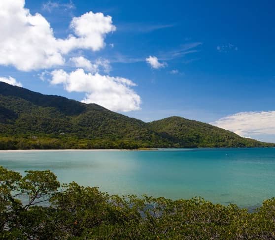 Cape Tribulation with ocean, rainforest, and mountains under a blue sky.