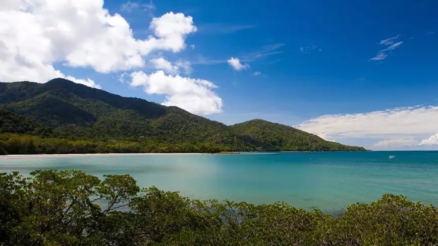 Cape Tribulation with ocean, rainforest, and mountains under a blue sky.