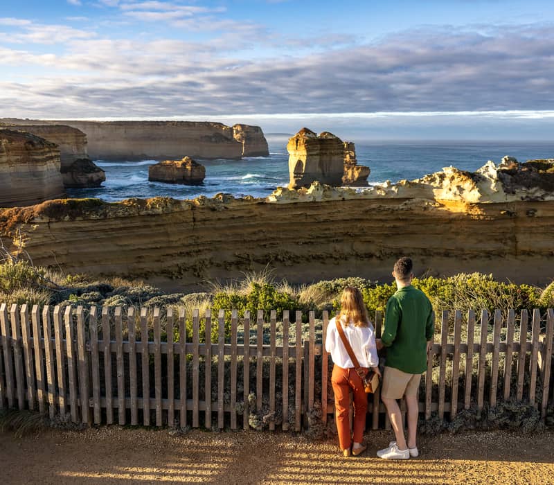 Two people standing at a lookout fence viewing The Razorback limestone stack on the Victoria coastline.