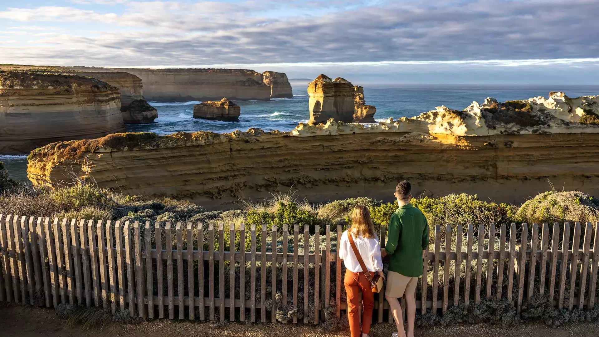 Two people standing at a lookout fence viewing The Razorback limestone stack on the Victoria coastline.