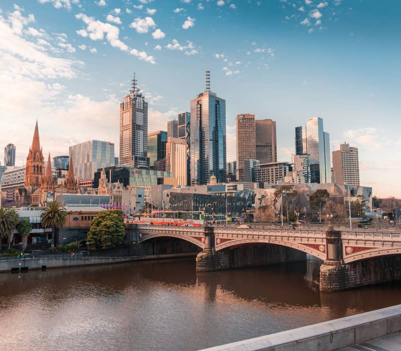 The stone arches of Princes Bridge over the Yarra River with the Melbourne city skyscrapers in the background.
