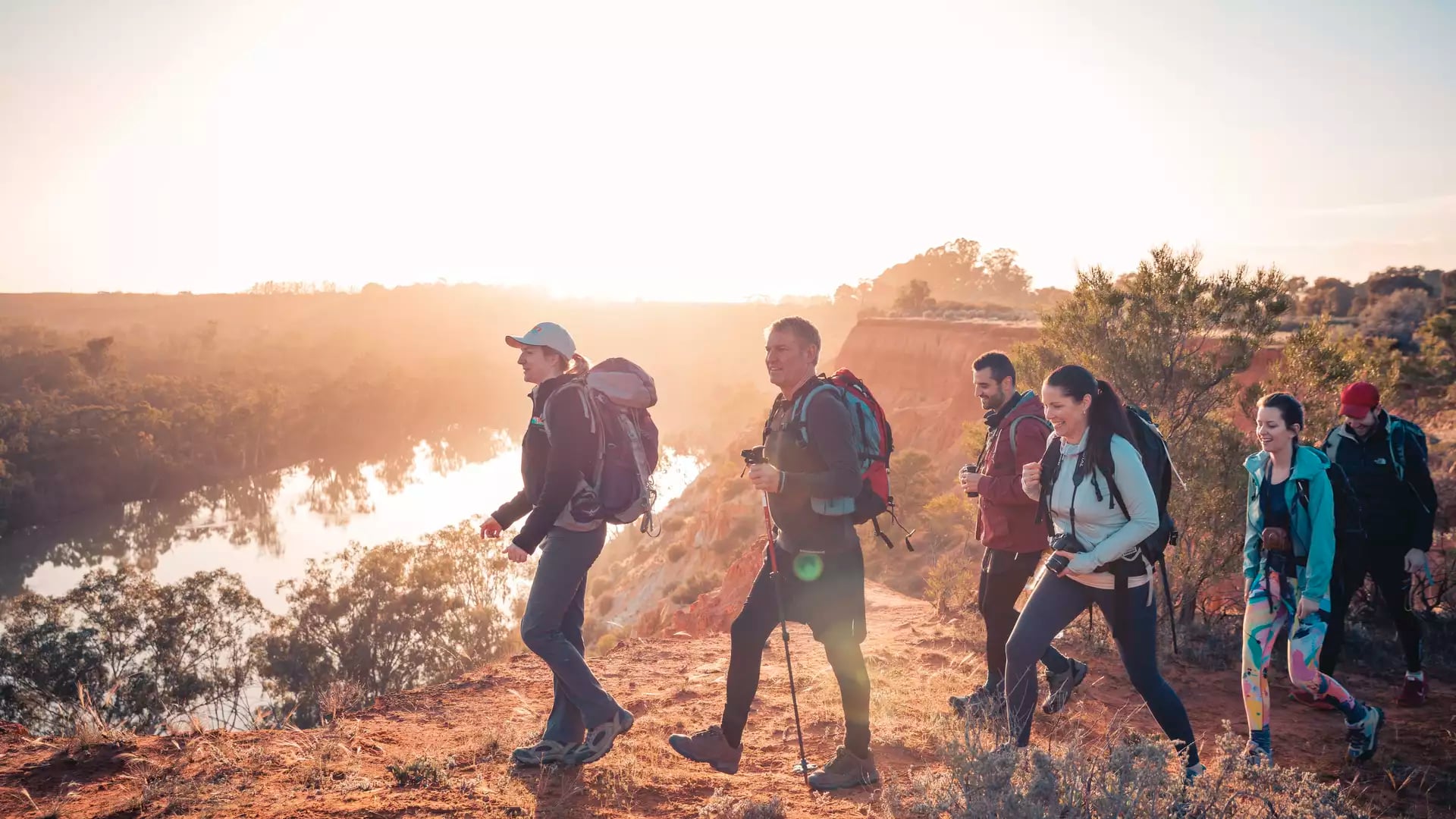 Silhouetted hikers walking along a cliff edge at sunset overlooking the Murray River.