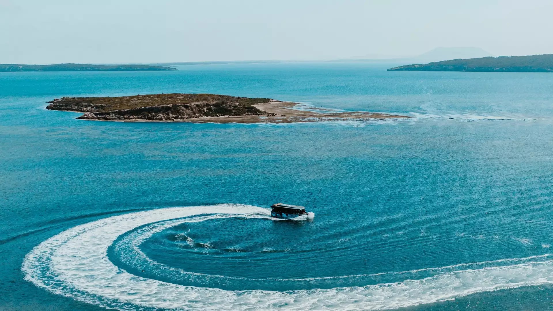 A black boat makes a sharp circular turn in bright blue water, leaving a white wake near Coffin Bay
