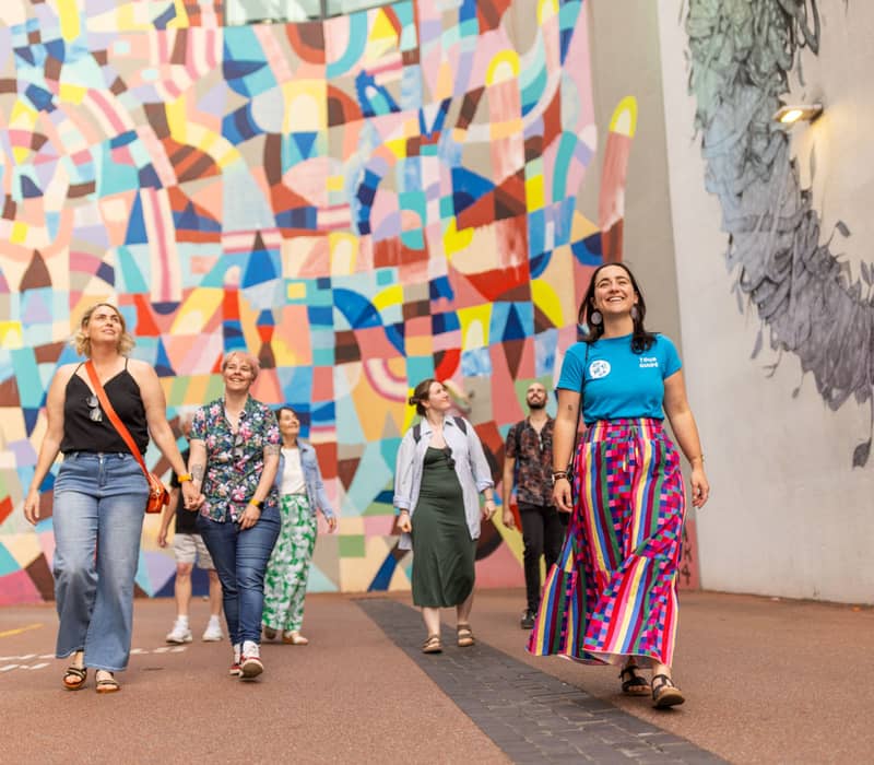 A diverse group of people walking and laughing in a Perth laneway featuring bright geometric wall murals.