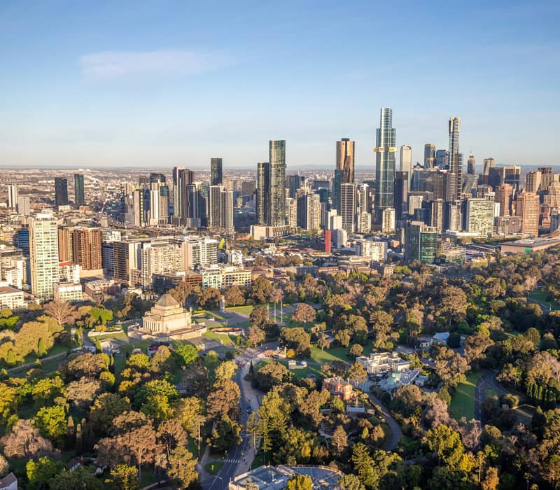 High-angle view of a large stone monument surrounded by green parkland with a dense city skyline in the background.